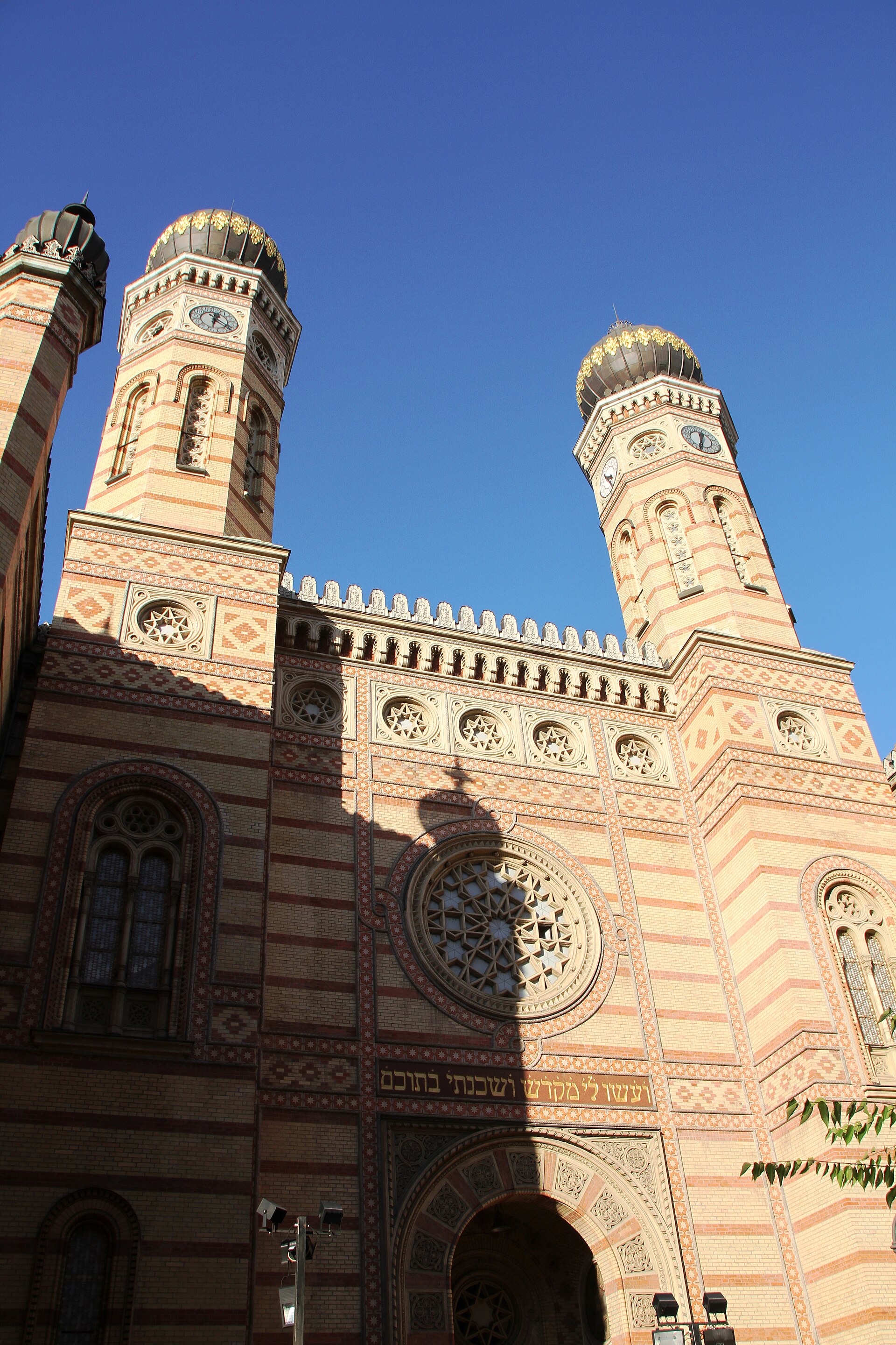 Interior of Dohány Street Synagogue in Budapest showing soaring architectural space with ornate details, stained-glass windows, and Byzantine-inspired tilework rendered in gold and colored geometric patterns