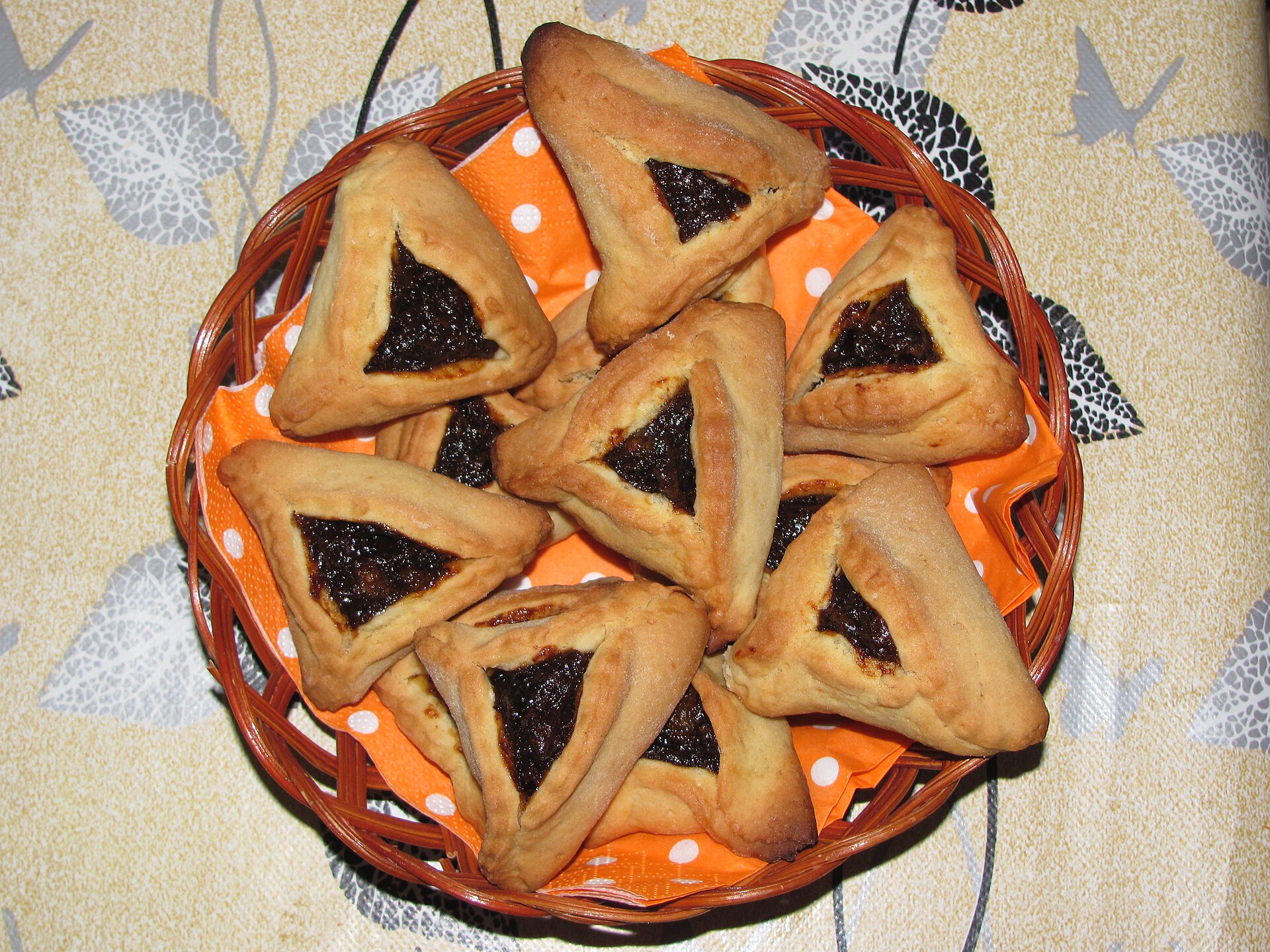 Homemade hamantaschen pastries filled with prune jam, arranged in a wicker basket with a polka-dot cloth