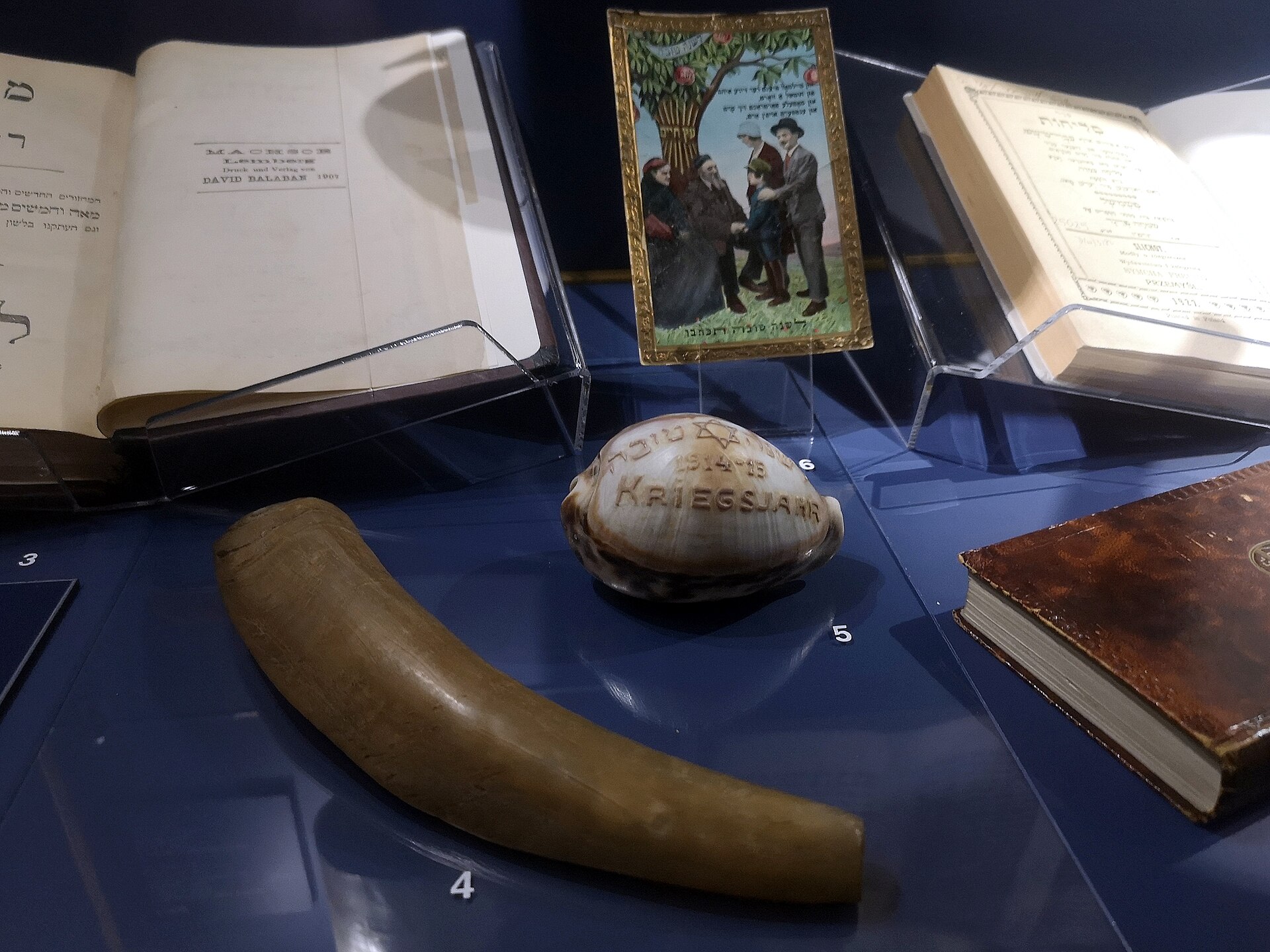 Museum display with a shofar, a vintage Rosh Hashanah greeting card, and High Holiday prayer books
