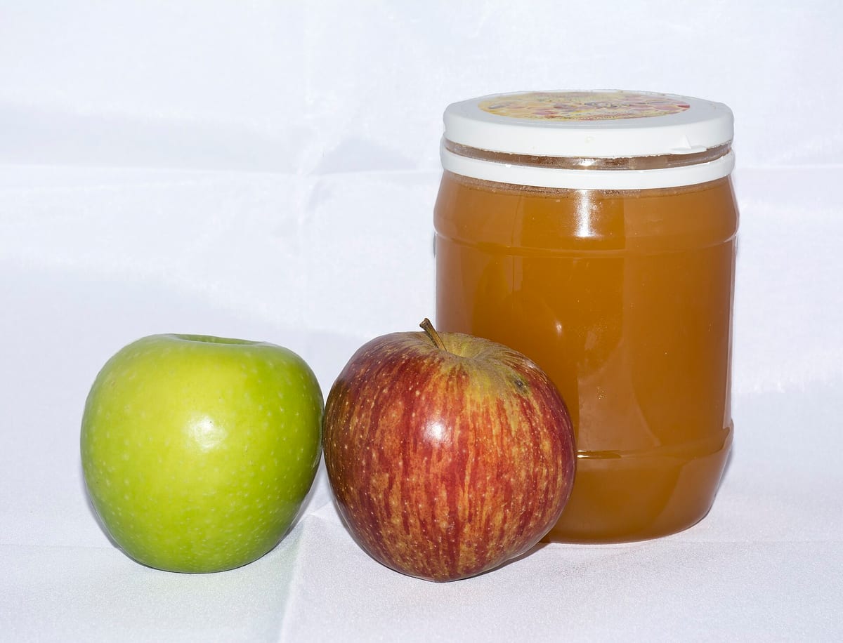 Two apples and a jar of honey, the classic Rosh Hashanah table pairing behind the "sweet year" greeting